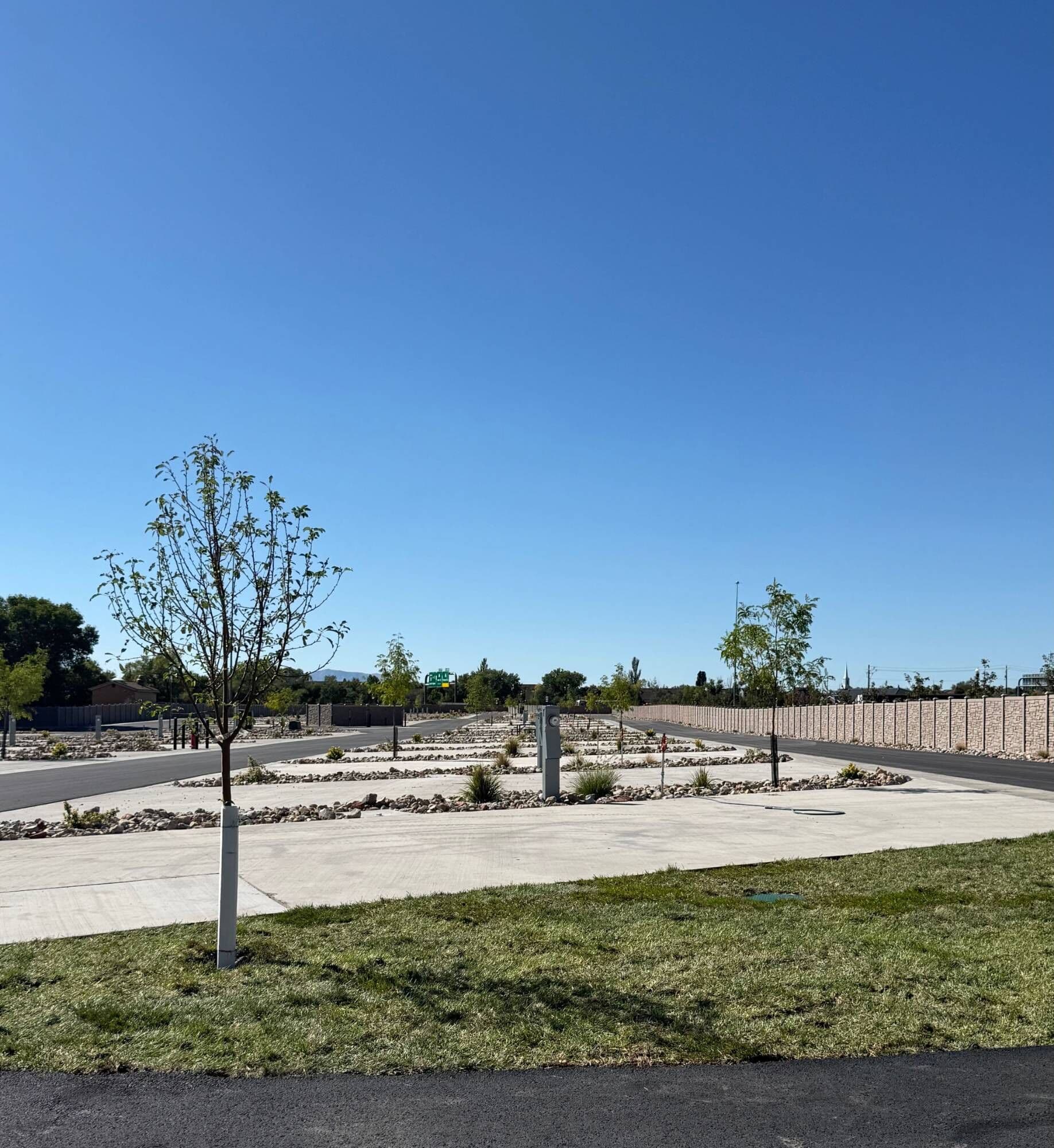 Rows of level concrete RV pads with full hookup pedestals, young trees, and rock landscaping at Spring Creek RV Resort